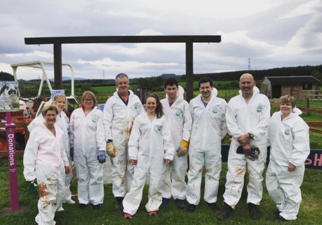 A group of people standing outside in a field wearing white boiler suits.