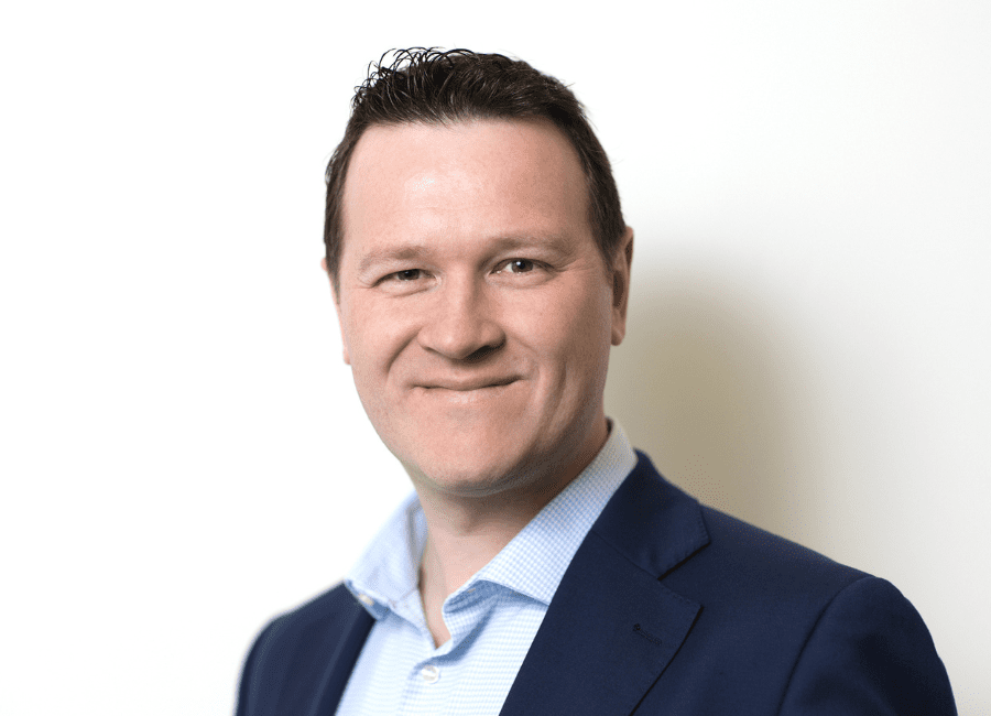 An image of Joel Topham wearing a black suit jacket with a blue shirt.