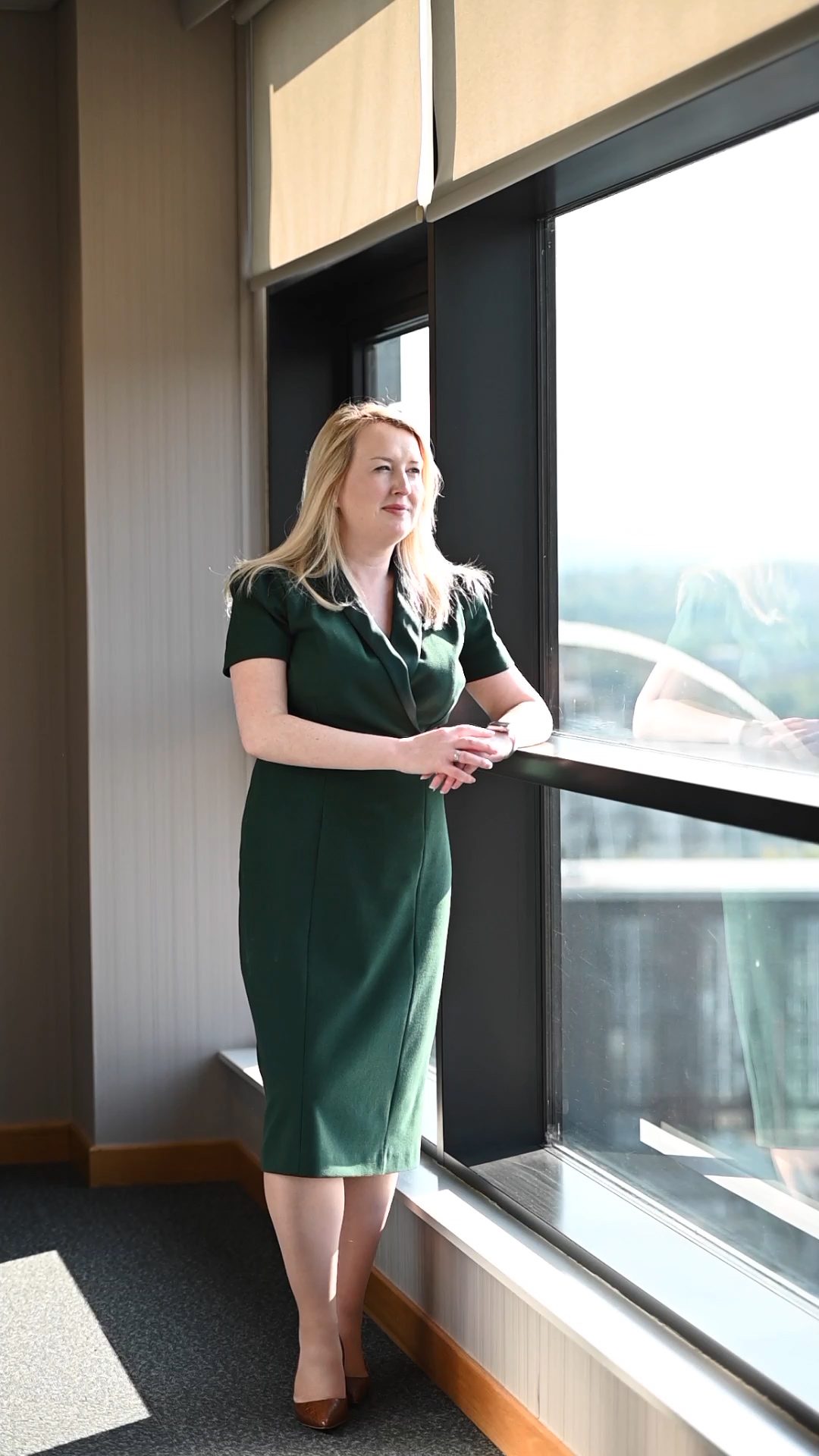 Louise McCosh Head of People Services and Partner standing by a window and wearing a green dress.