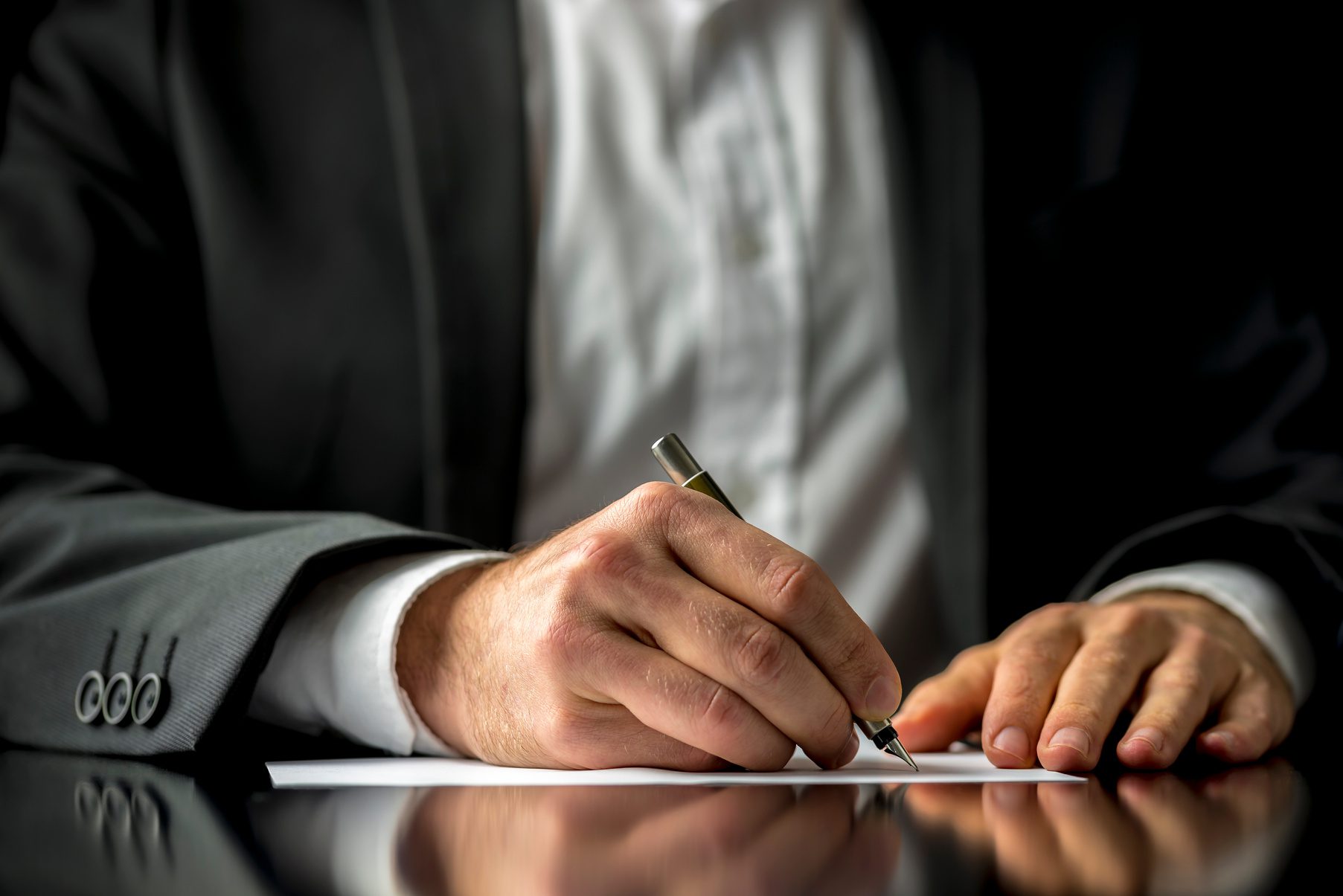 A person writing on a paper wearing a shirt and blazer.