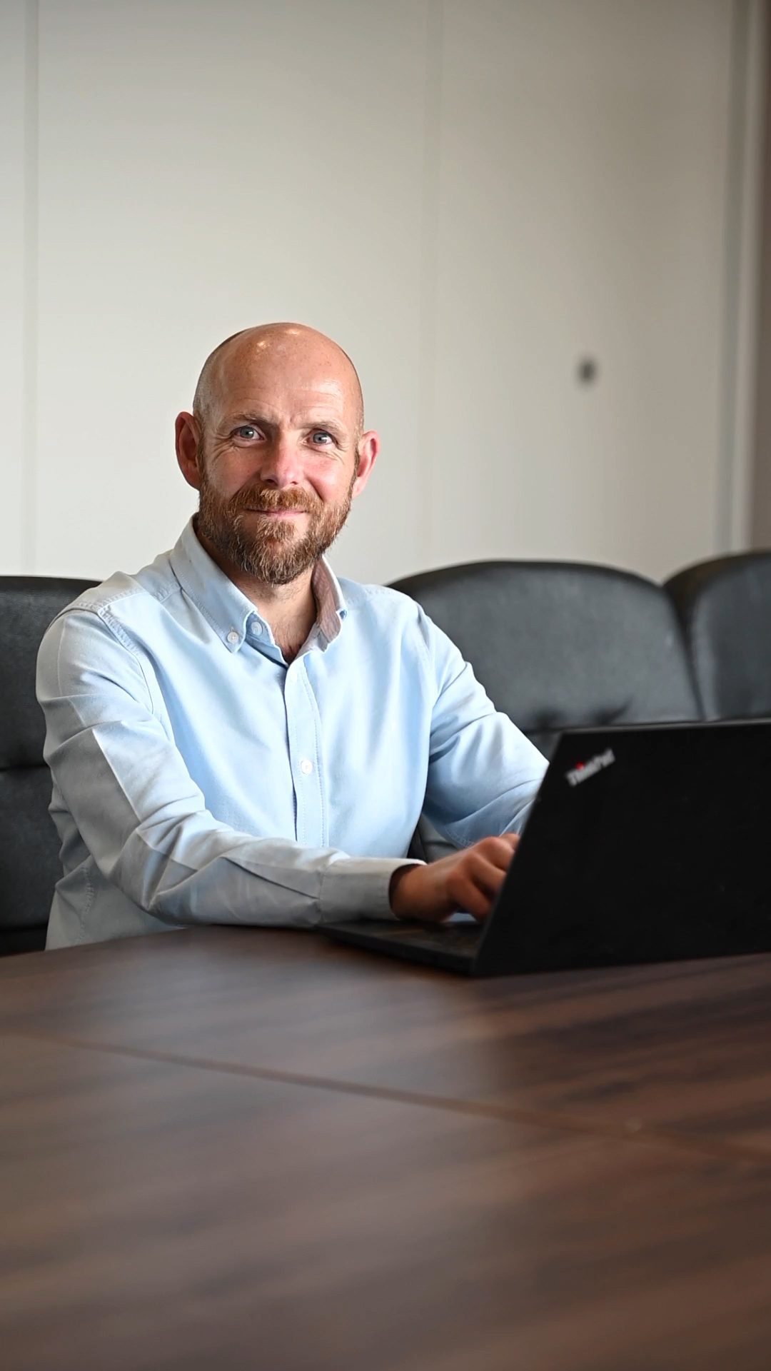 An image of Mark Girvan sitting at a desk with his laptop and wearing a blue shirt.