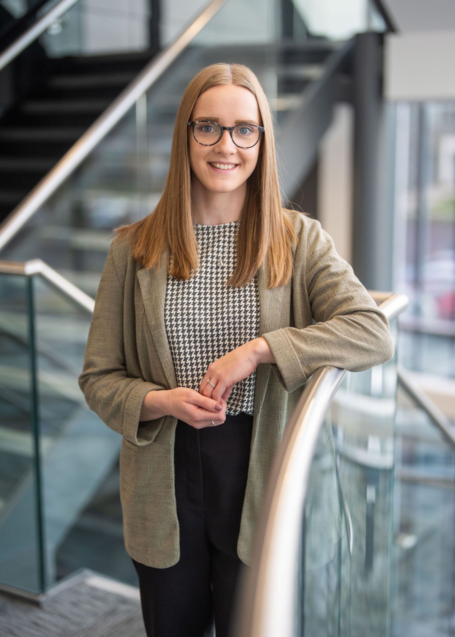 An image of Amber Clouston standing on the stairs in the Aberdeen office. She has her hands together and is smiling at the camera.