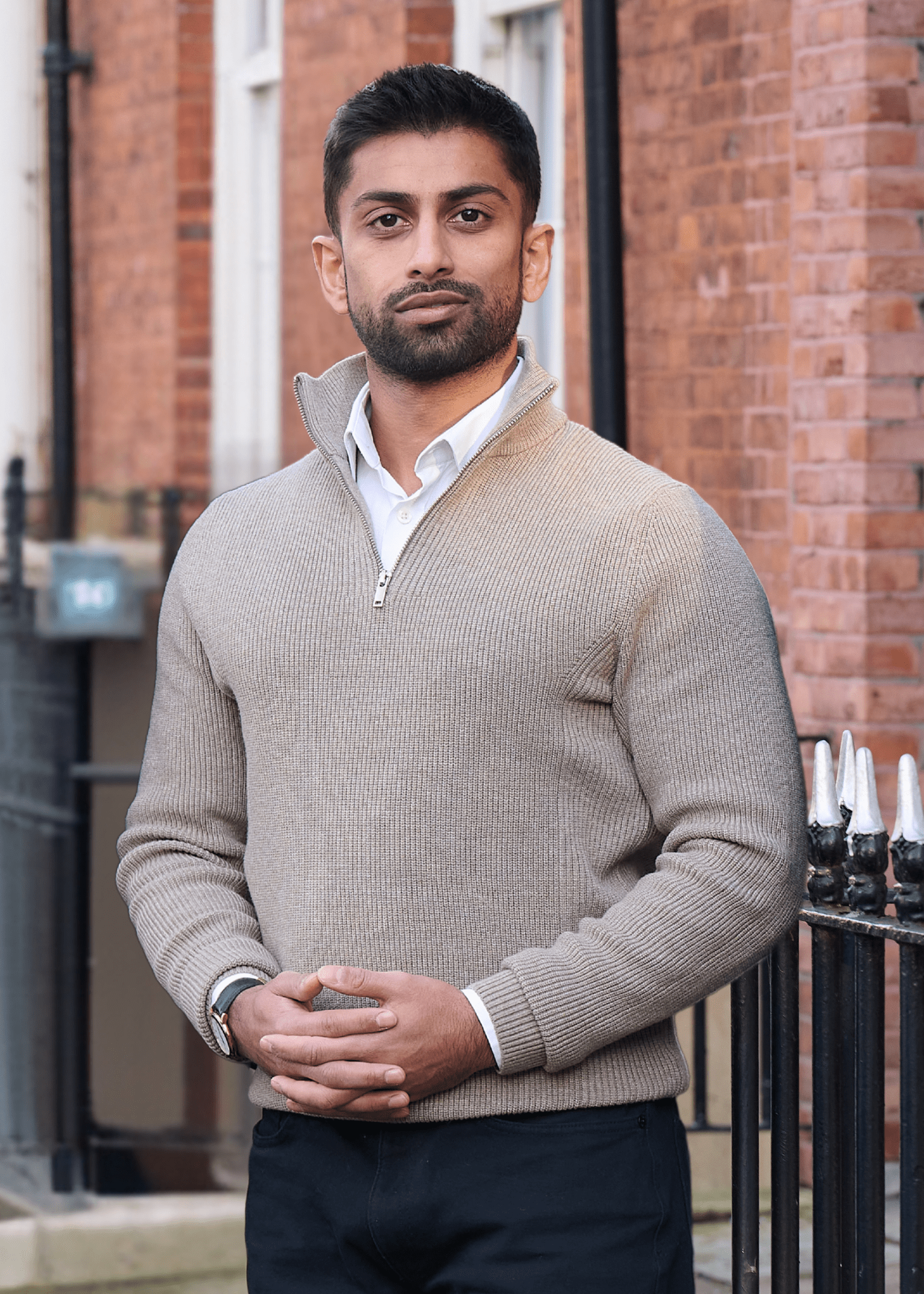 An image of Abdullah Daji wearing a cream top and standing outside a building smiling at the camera.